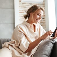 Une femme souriante aux cheveux attachés est assise sur le canapé et les touches du téléphone