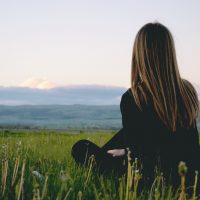 femme assise sur l'herbe en regardant la montagne