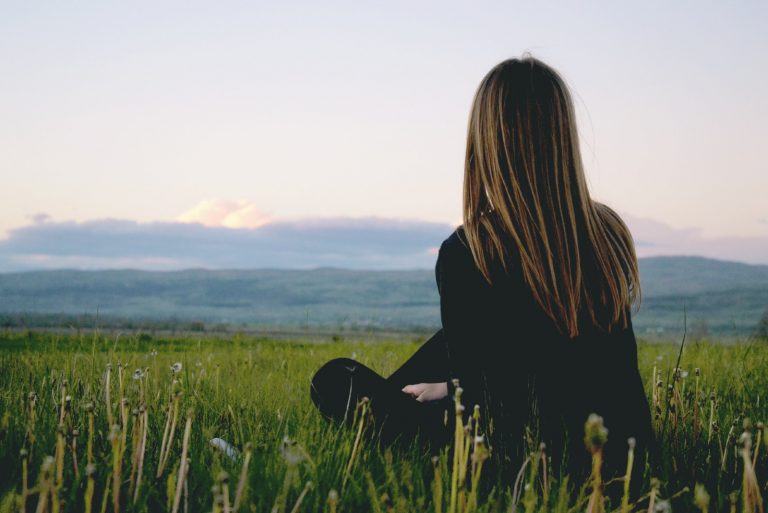 femme assise sur l'herbe en regardant la montagne