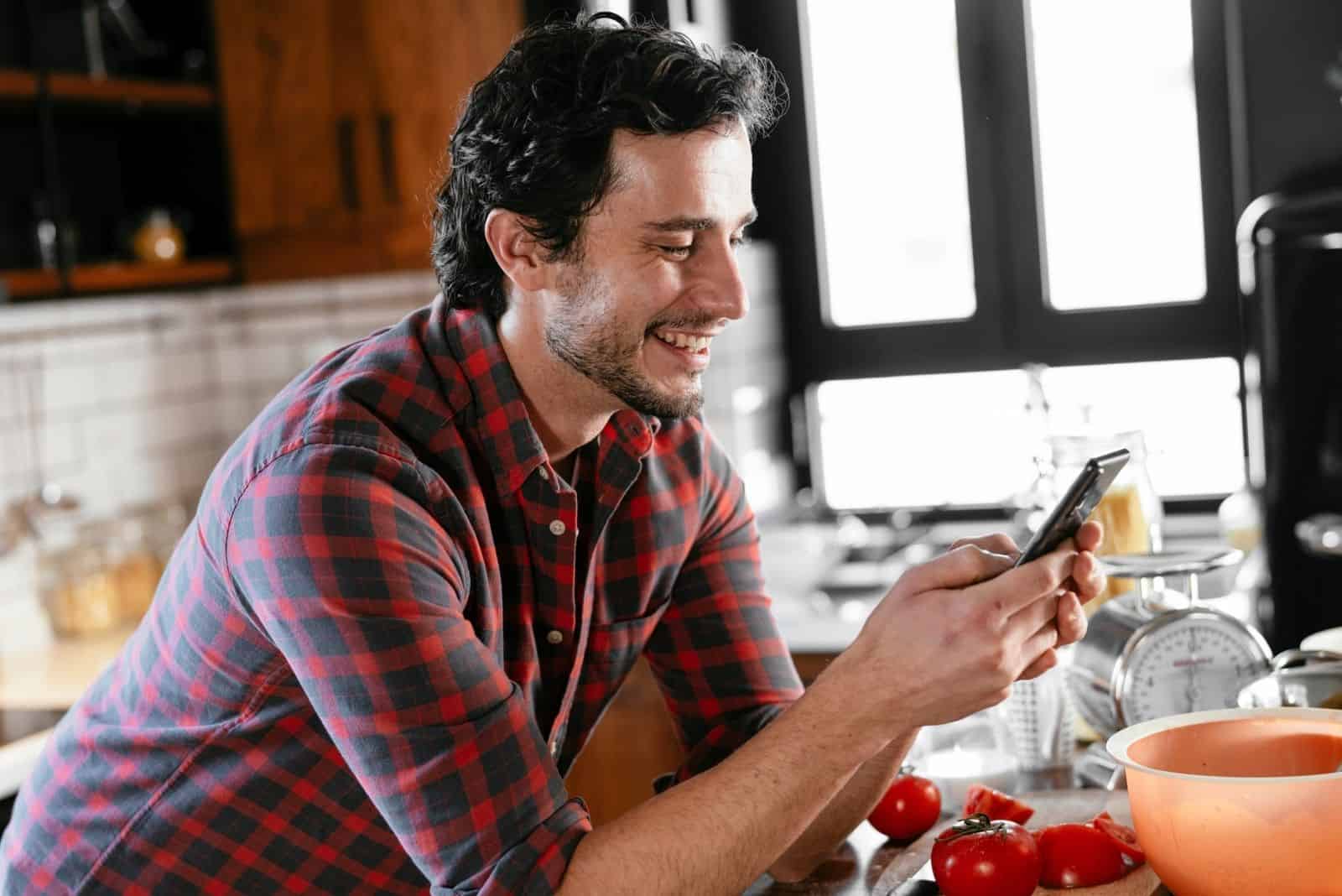 Jeune homme préparant le petit-déjeuner et utilisant le téléphone