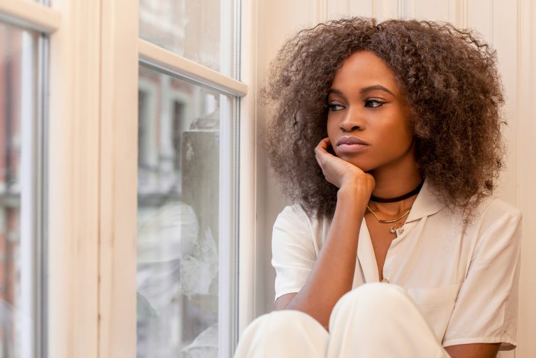 femme triste aux cheveux bouclés assis près de la fenêtre