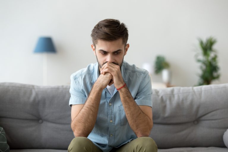 homme triste en chemise bleue assis sur un canapé