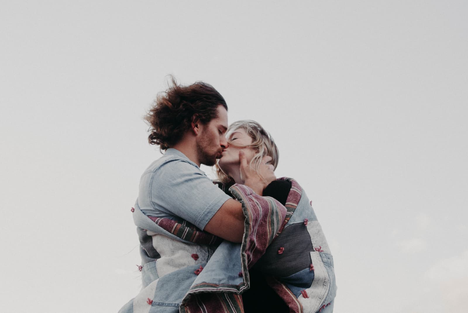 homme et femme enveloppés dans une couverture s'embrasser en plein air