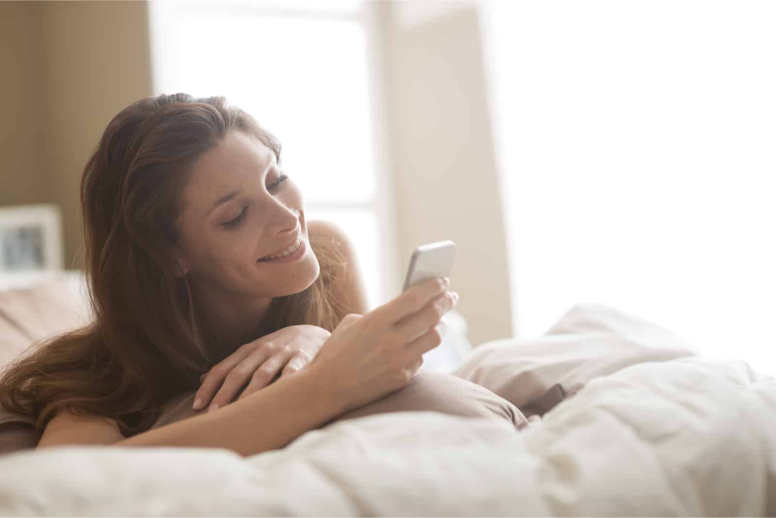 femme regardant son smartphone en étant allongée sur un lit