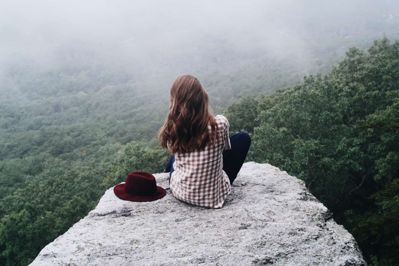 femme assise sur un rocher près de chapeau en regardant les arbres