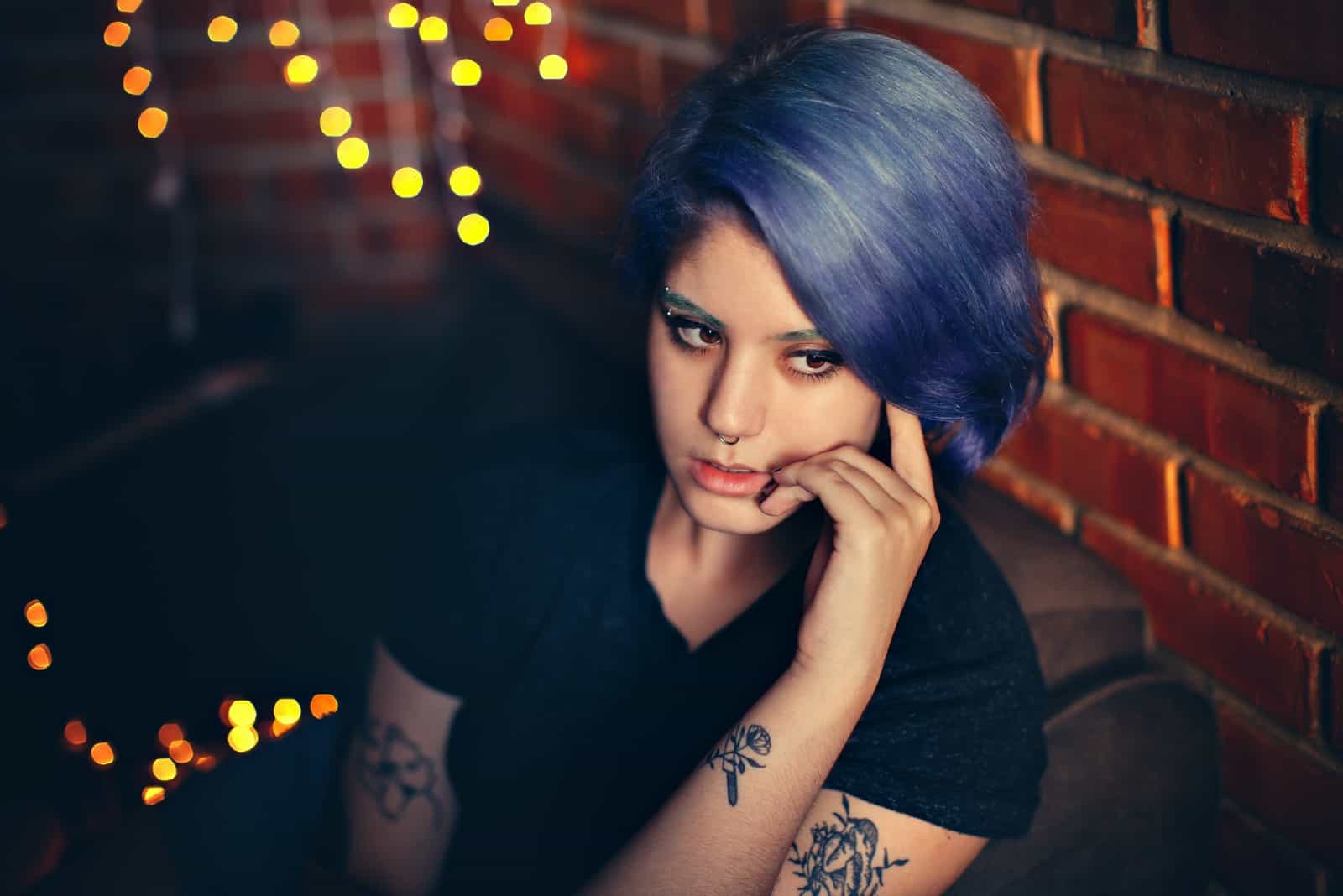 femme pensive aux cheveux violets assis près du mur