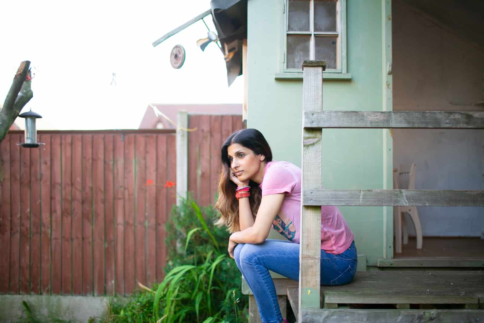 femme pensive en t-shirt rose assis près du mur
