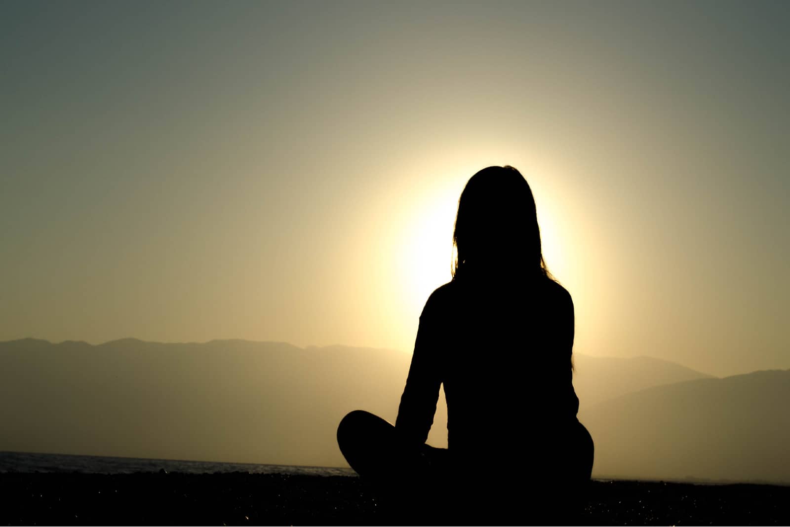 femme assise sur la plage pendant le coucher du soleil