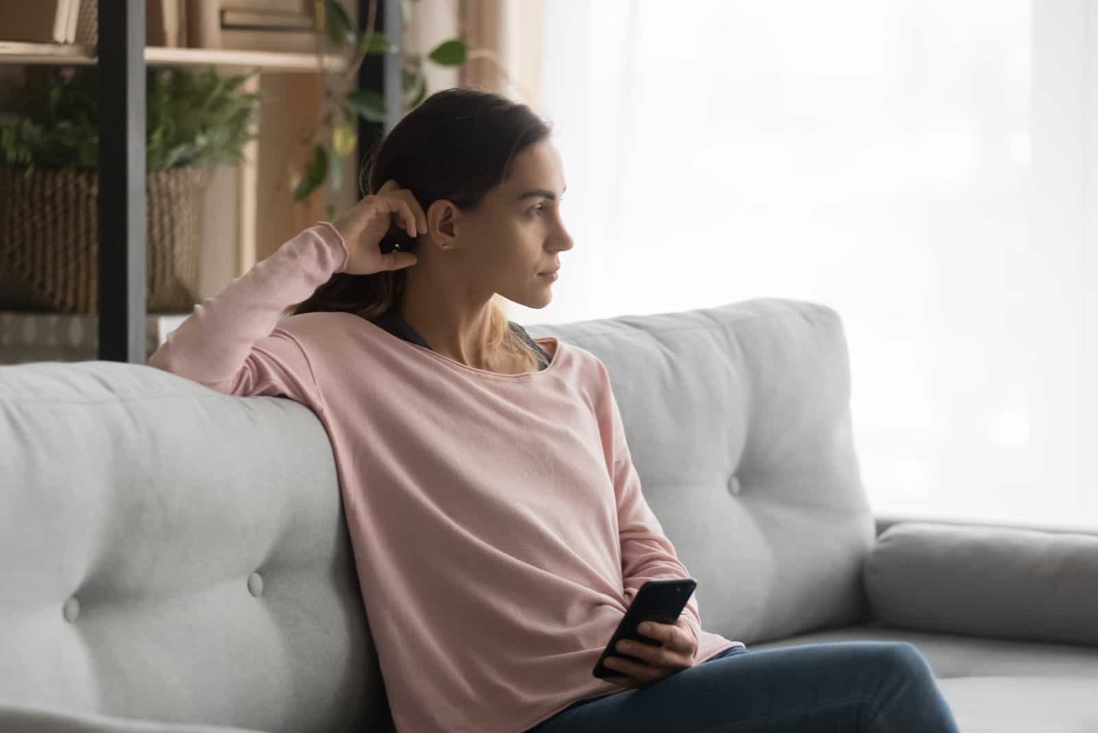 femme assise sur un canapé confortable dans le salon regarde à distance