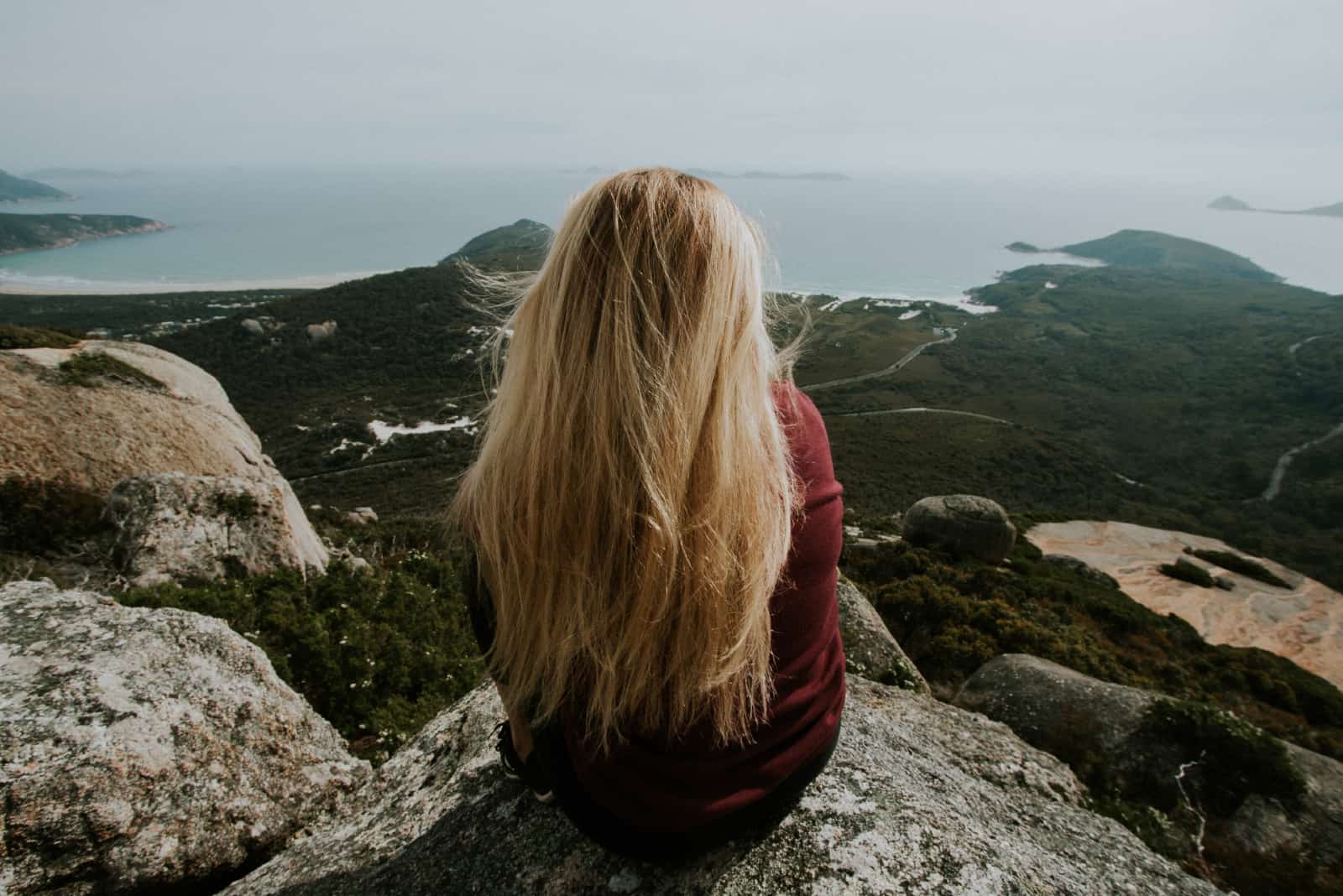 femme blonde assise sur un rocher en regardant l'océan