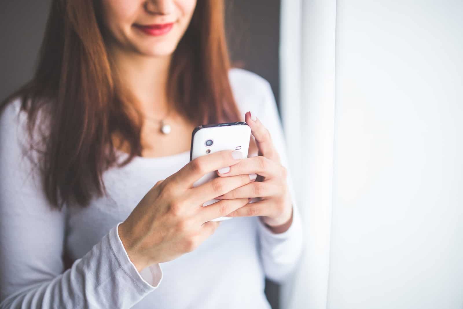 femme utilisant un smartphone alors qu'elle se tient près d'un rideau