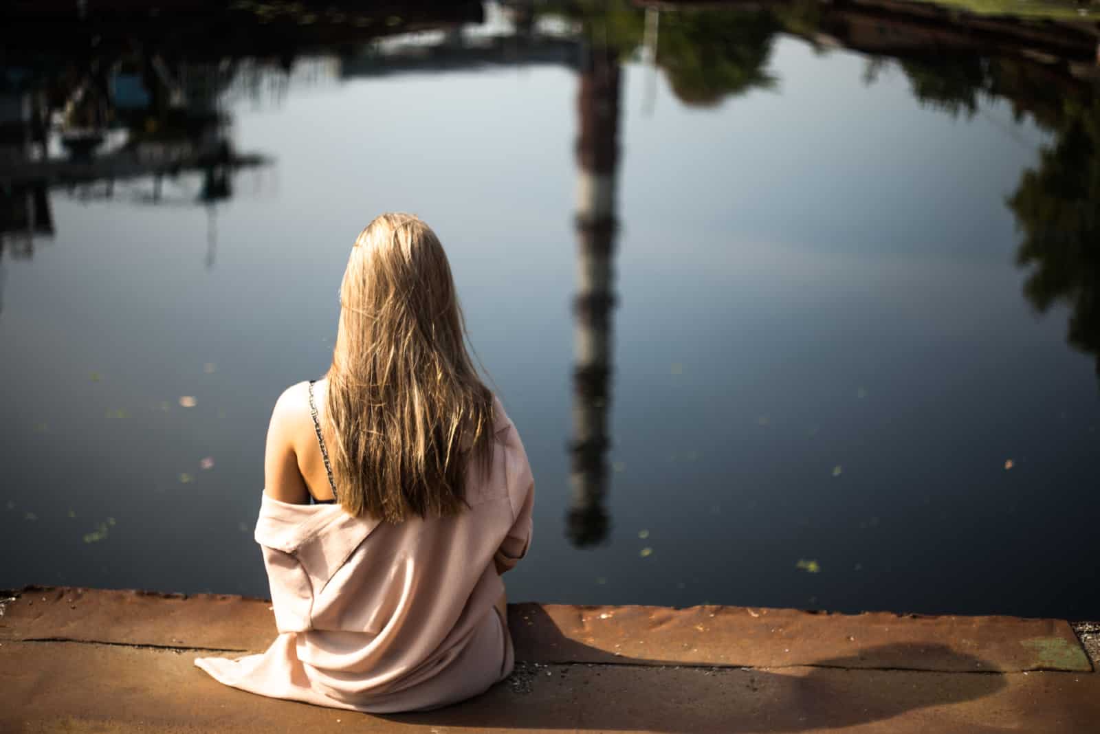 Femme blonde assise sur une surface en béton en regardant le lac
