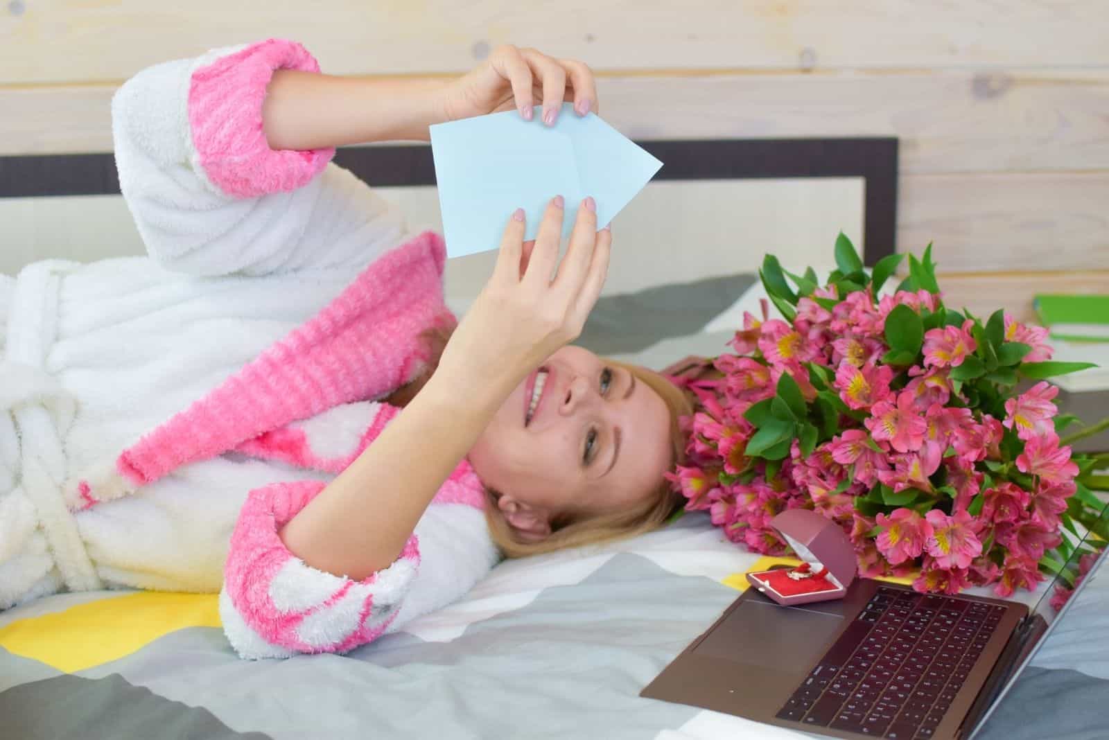 Heureuse belle femme lit lettre d'amour au lit avec un bouquet de fleurs
