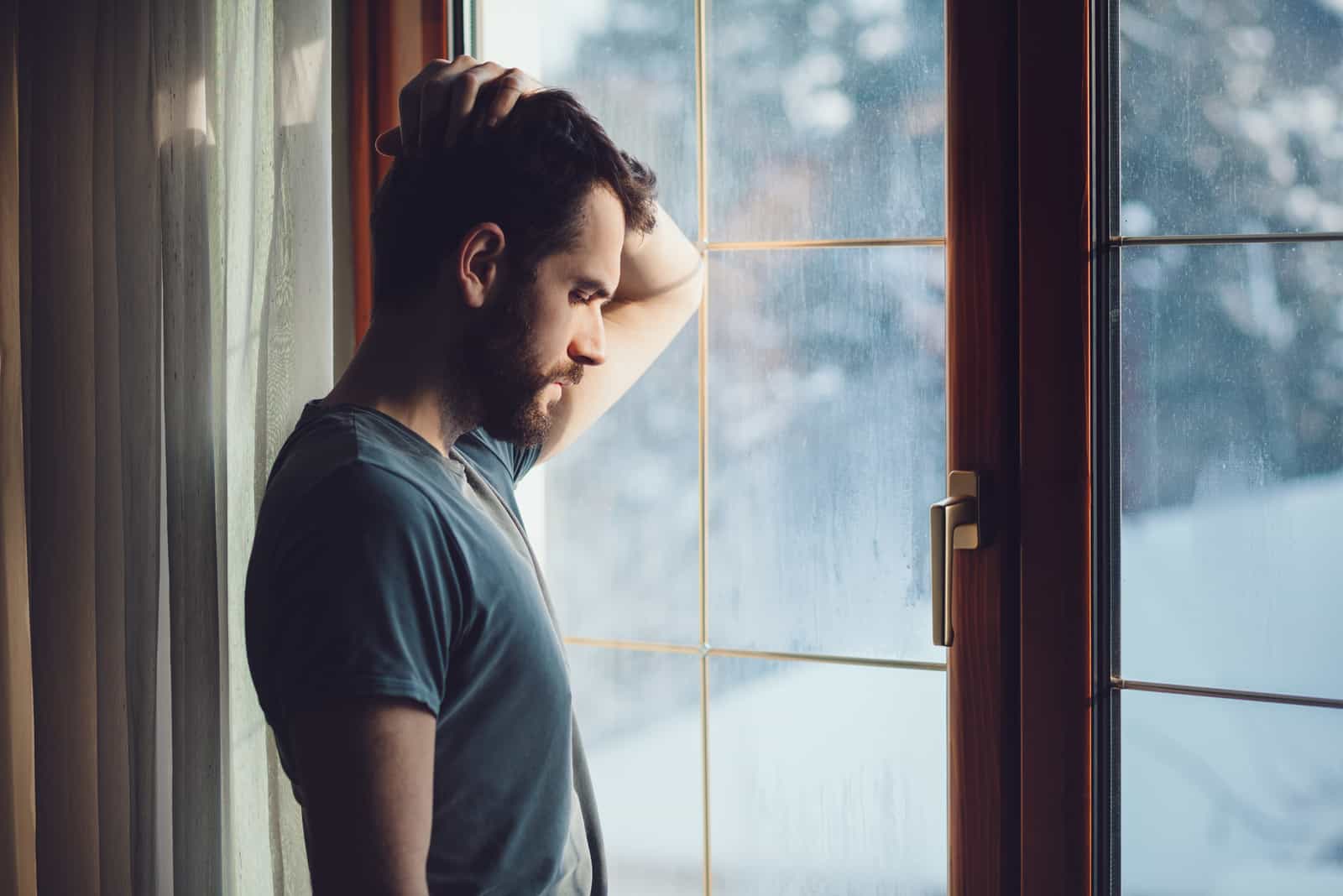 homme triste touchant sa tête en se tenant près de la fenêtre