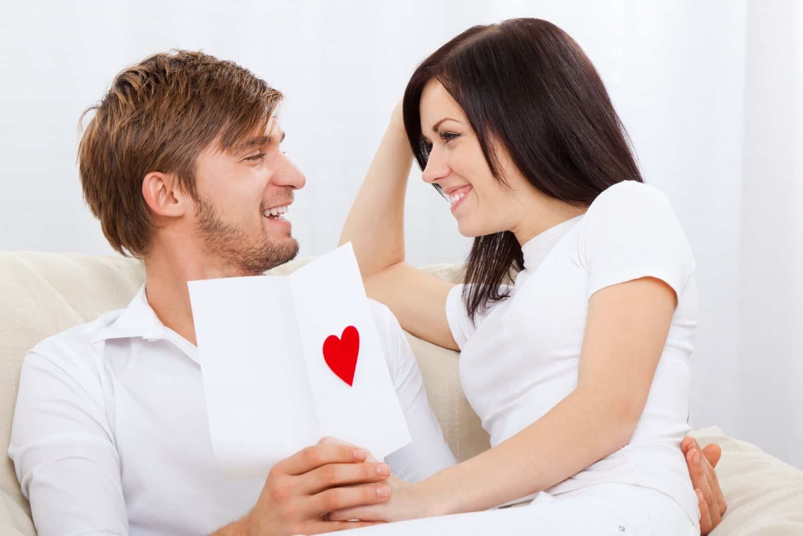 jeune couple d'amoureux tenant une carte de vœux de la Saint-Valentin avec un cœur rouge