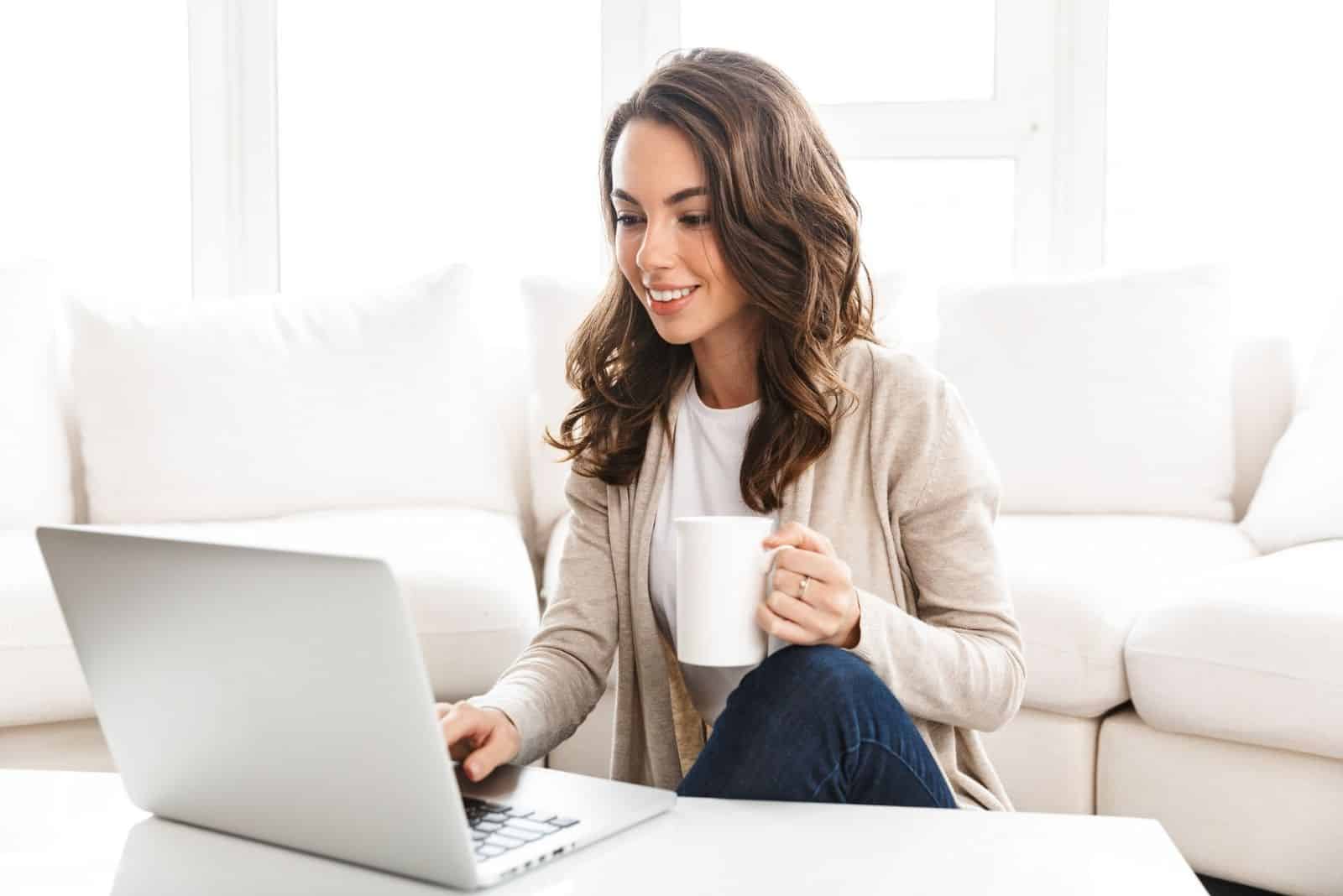 Jeune femme travaillant sur un ordinateur portable alors qu'il était assis dans le salon, buvant du café