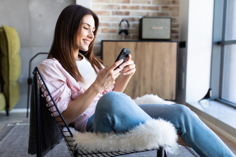 femme heureuse regardant son téléphone tout en étant assise sur une chaise