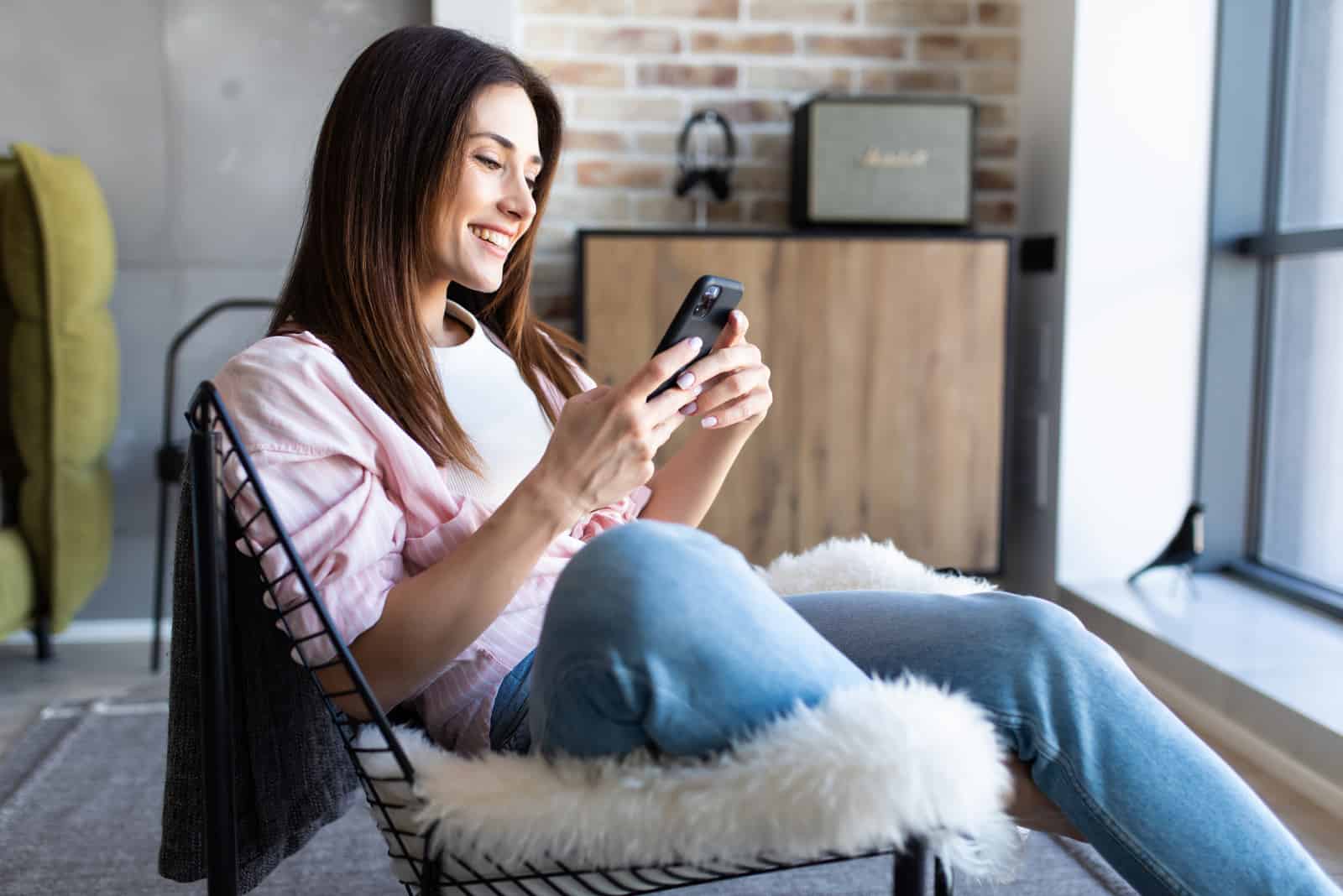 femme heureuse regardant son téléphone tout en étant assise sur une chaise