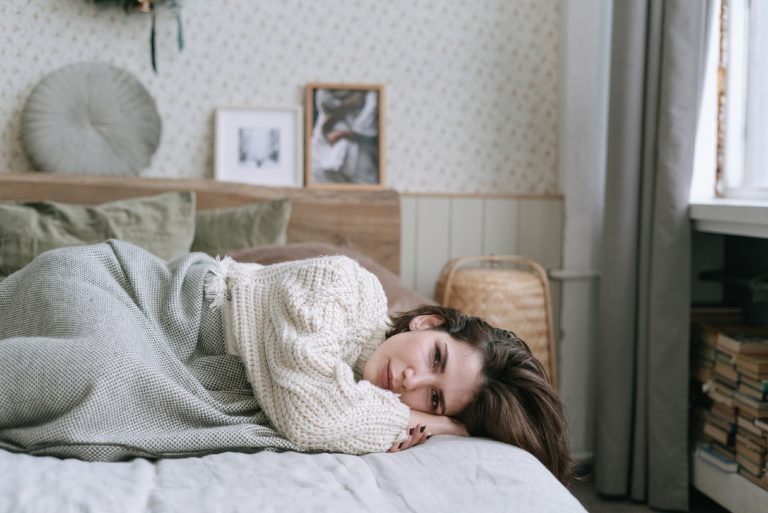 femme triste en chandail blanc allongée sur un lit