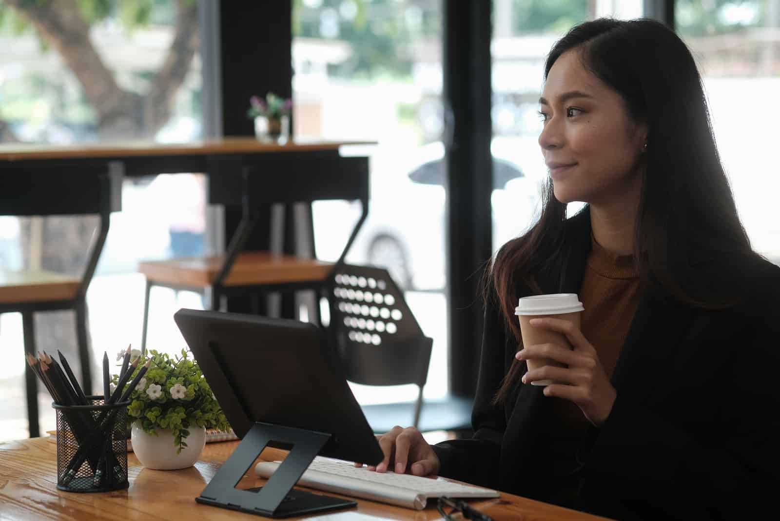 Vue latérale d'une femme d'affaires tenant une tasse de café et utilisant une tablette dans un café.