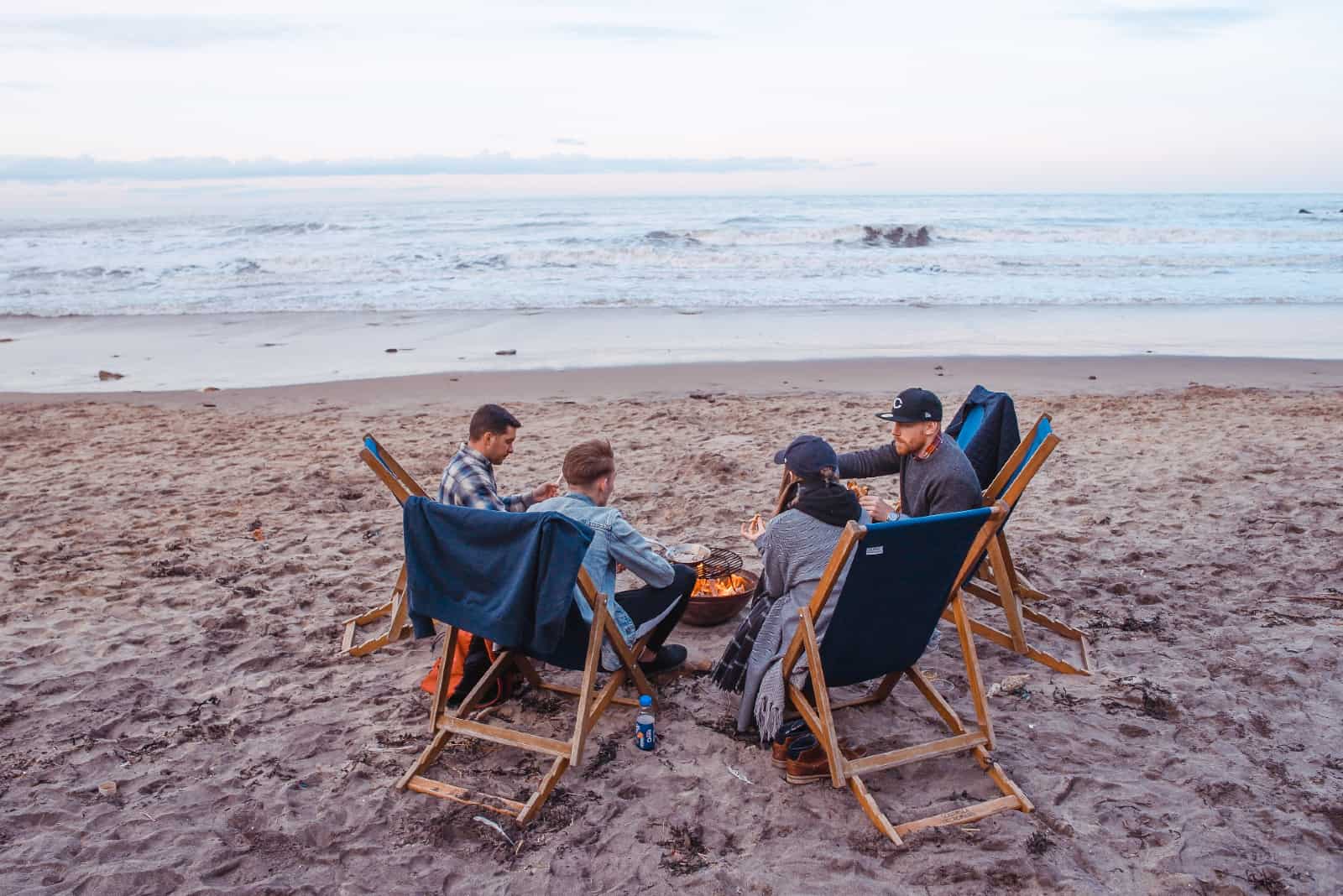 quatre amis assis sur la plage près d'un feu de camp