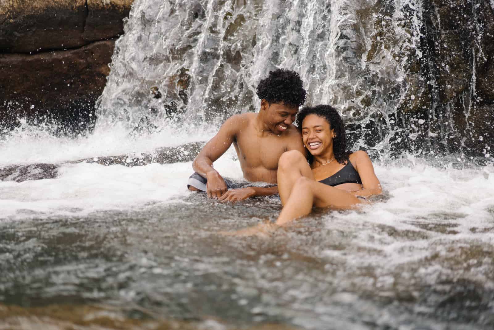 homme et femme souriant assis près d'une chute d'eau