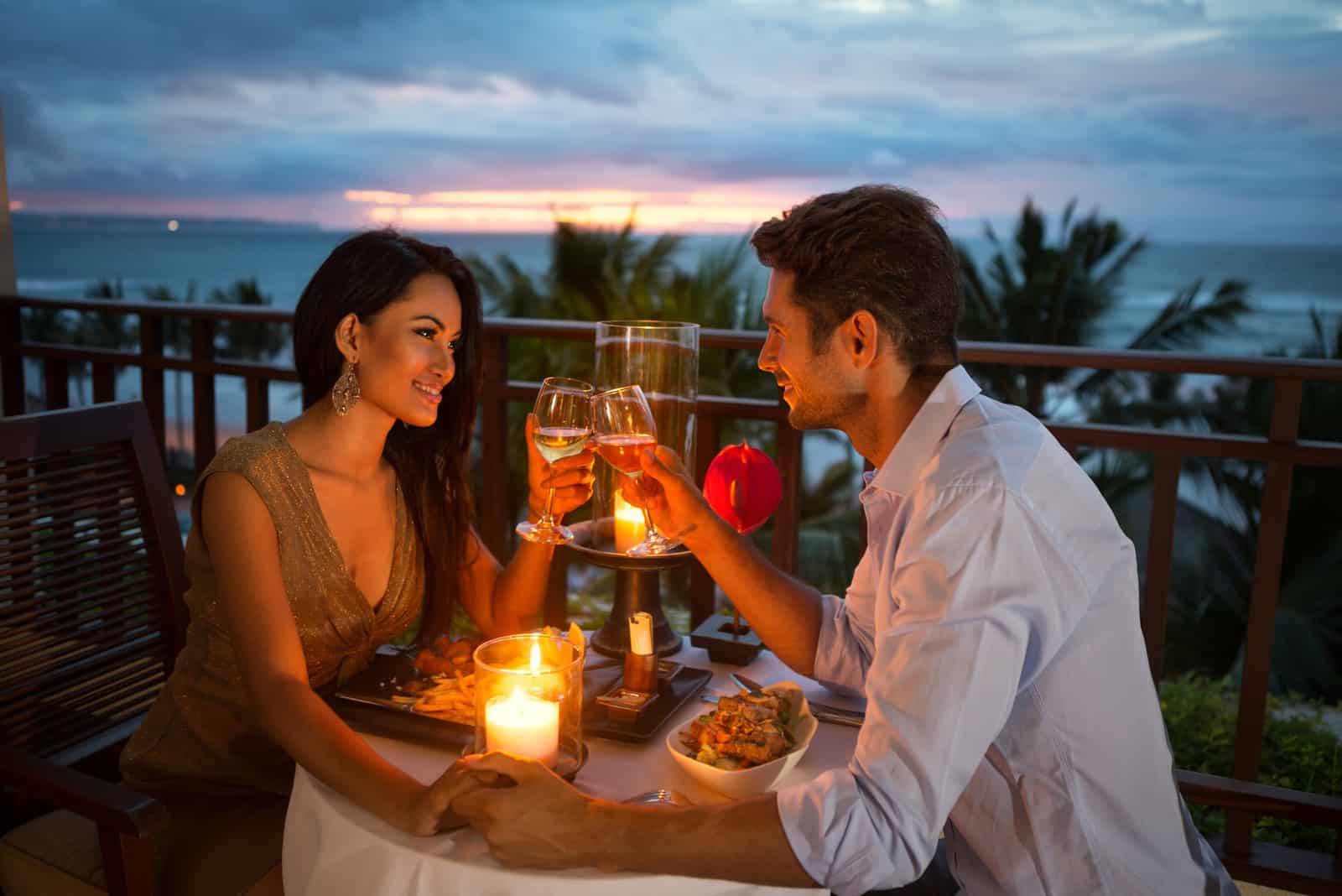 homme et femme trinquant avec du vin assis sur une terrasse