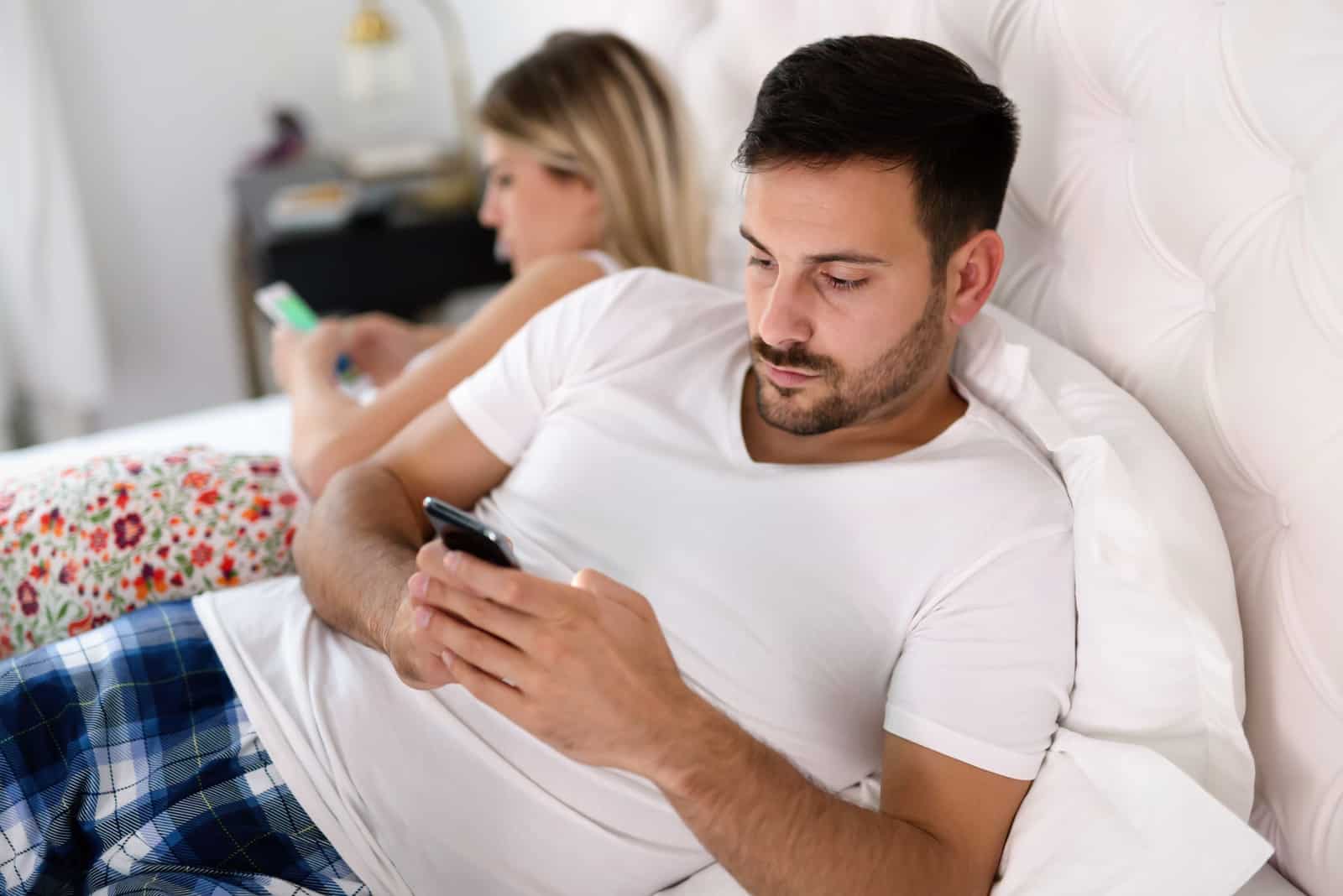 homme et femme utilisant des smartphones au lit