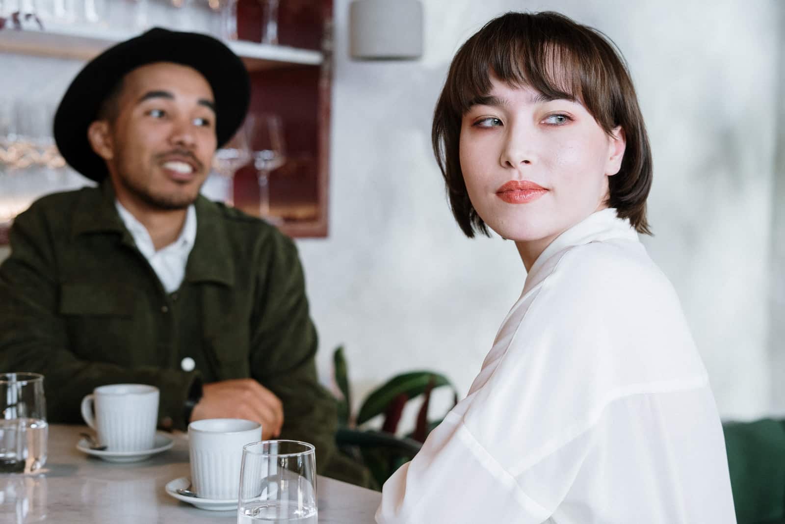 femme en chemise blanche assise dans un café près d'un homme