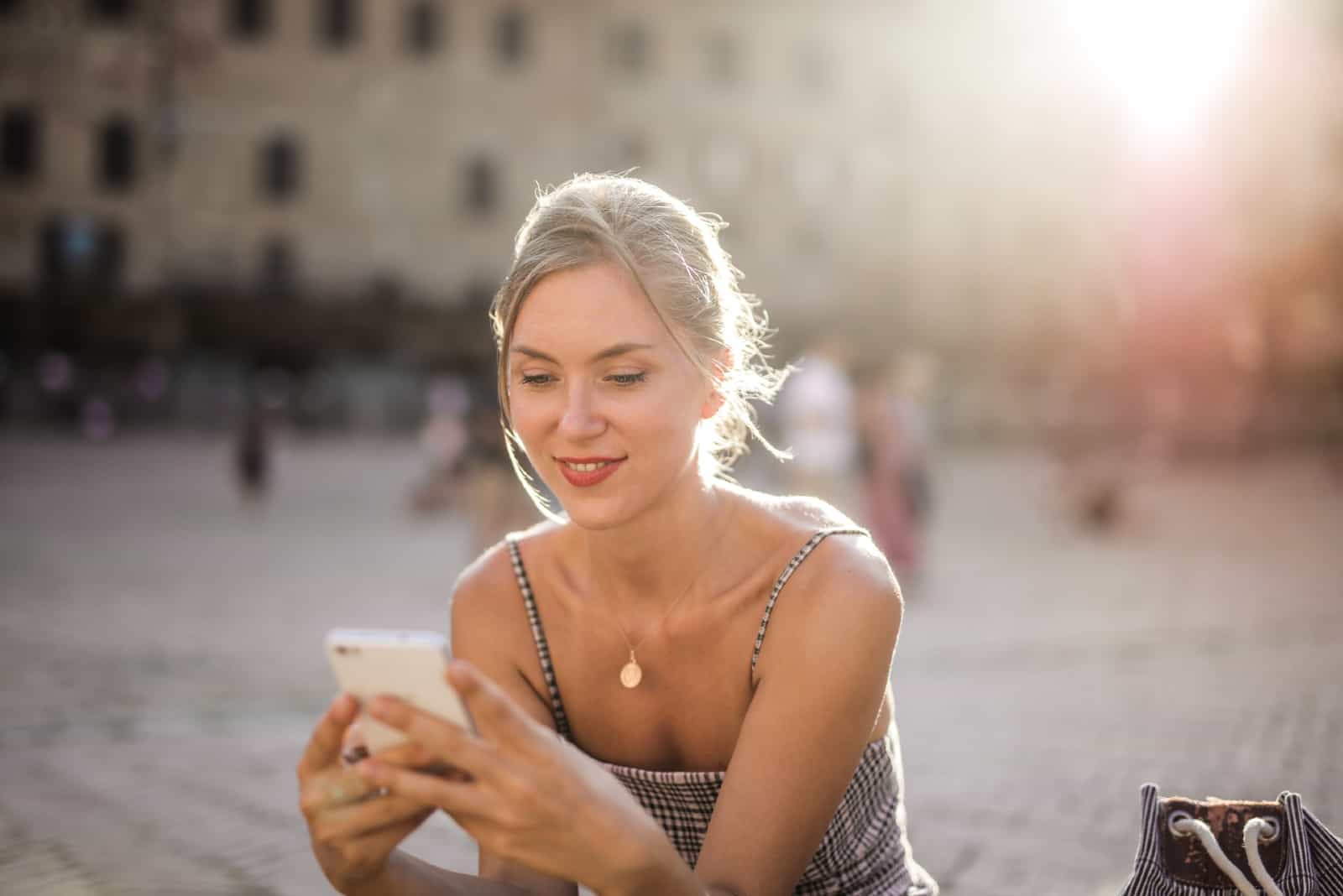 femme heureuse utilisant un smartphone tout en étant assise à l'extérieur