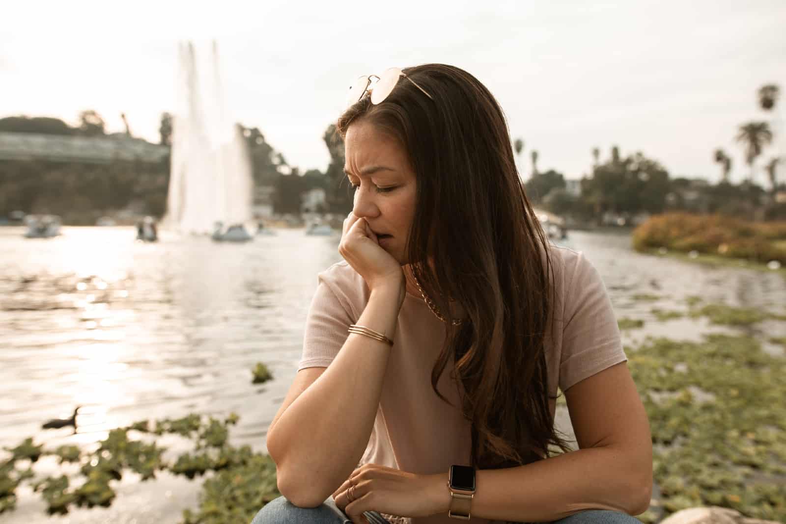 femme triste avec un bracelet doré assise près de l'eau