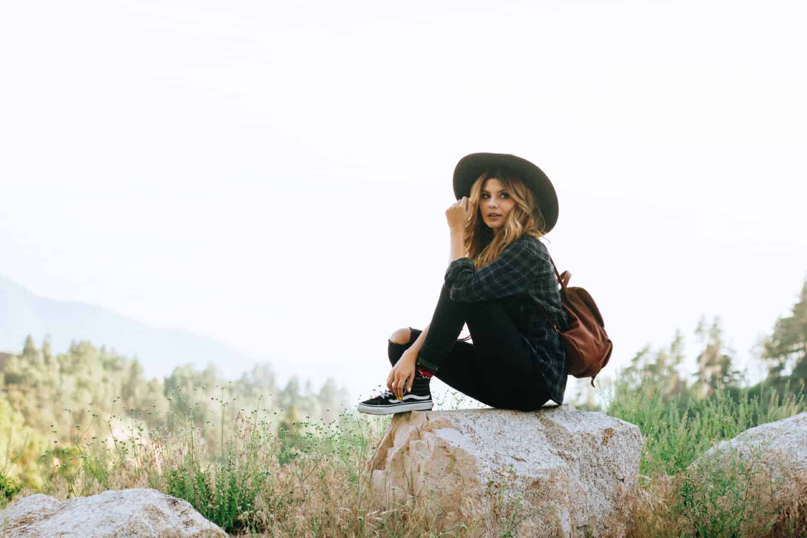 femme avec un chapeau noir assise sur un rocher