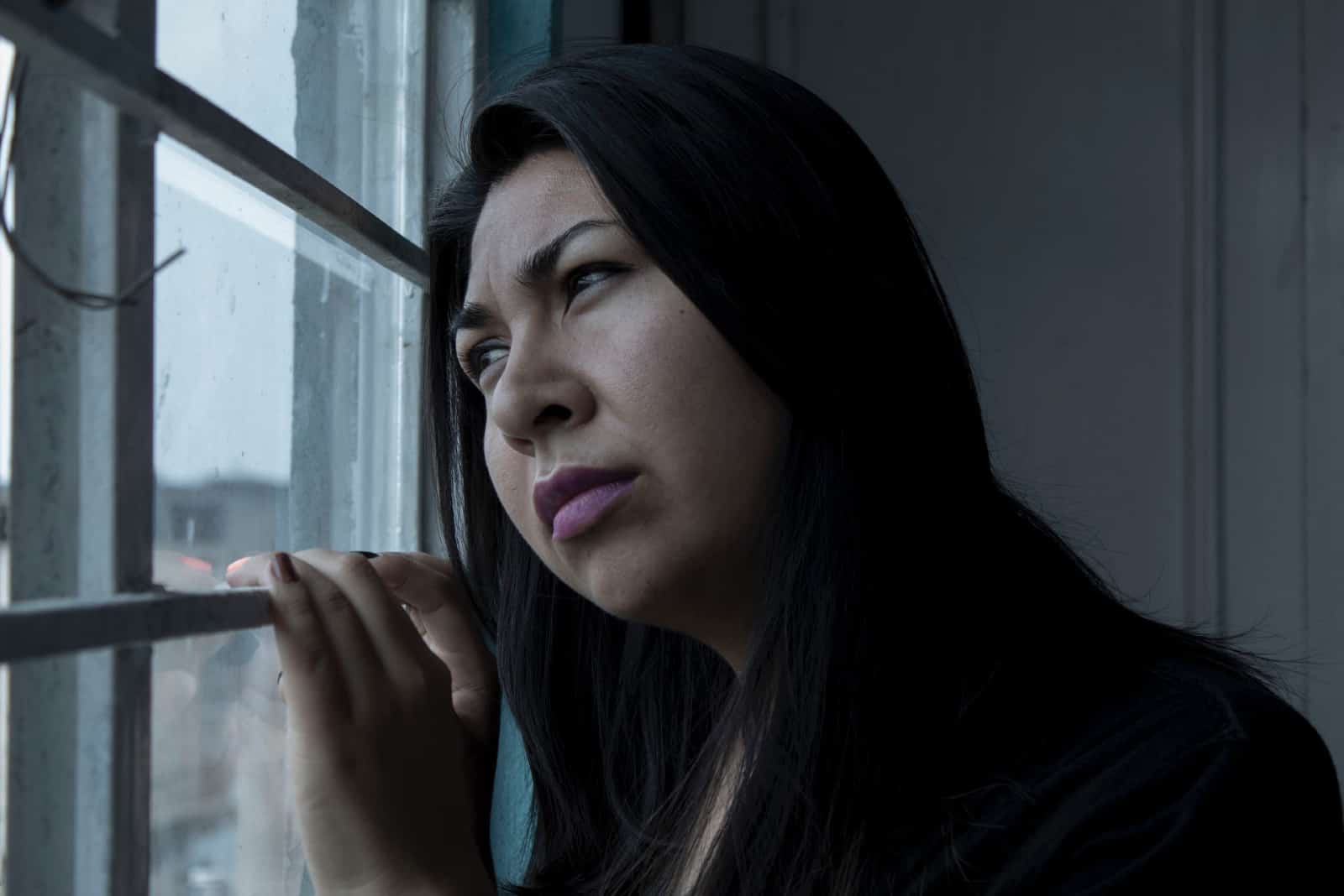femme triste en chemise noire debout près d'une fenêtre