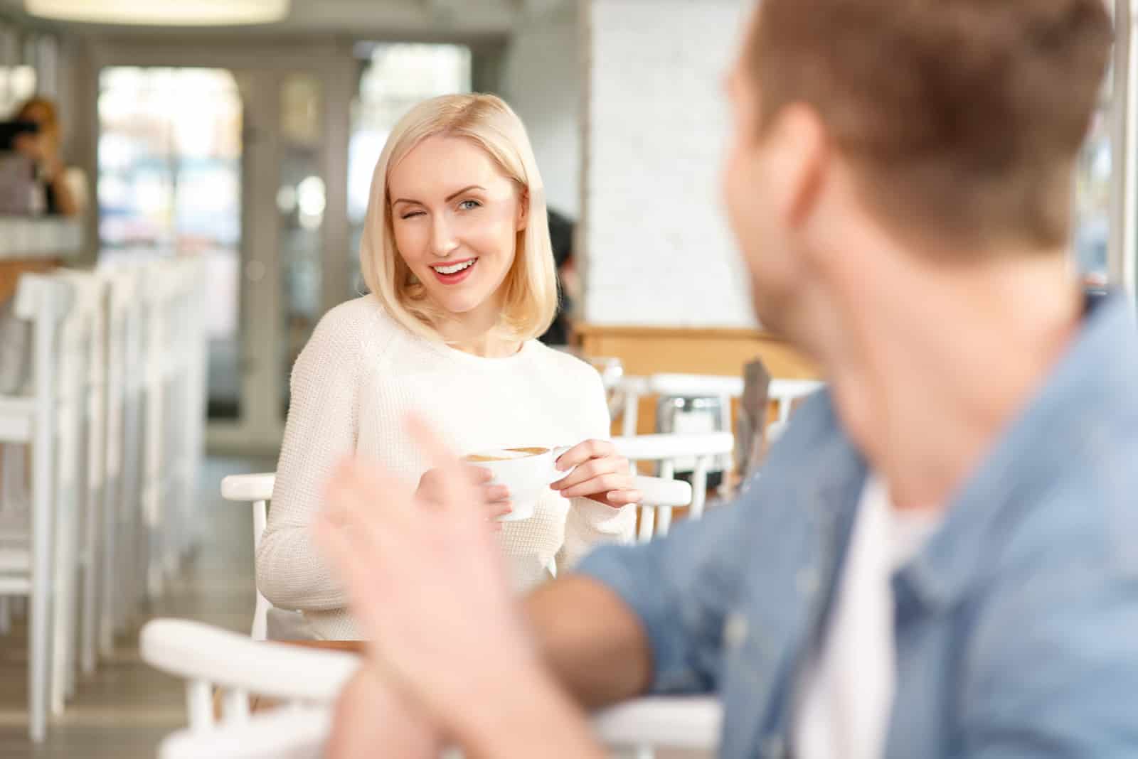 Une femme fait un clin d'œil à un homme assis dans un café