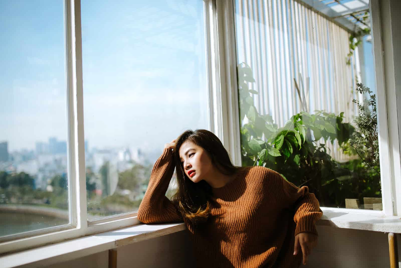 femme triste en pull brun regardant par la fenêtre