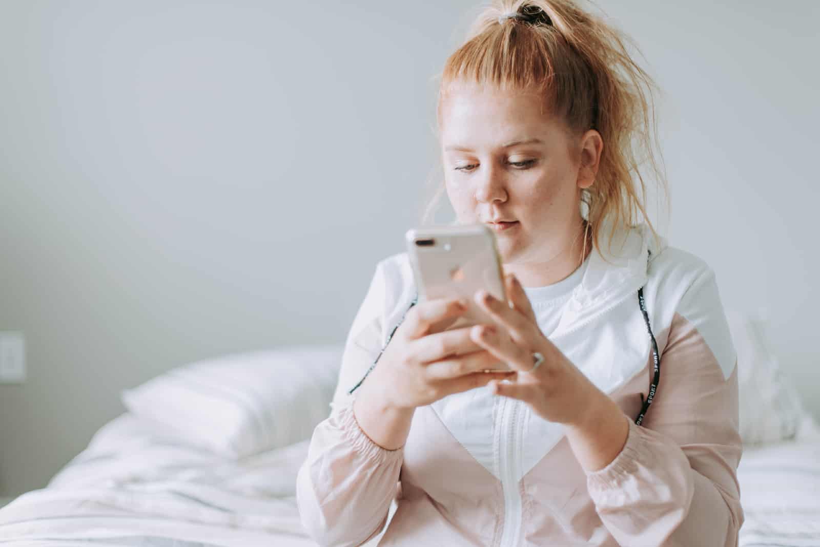 femme regardant son smartphone assise sur un lit