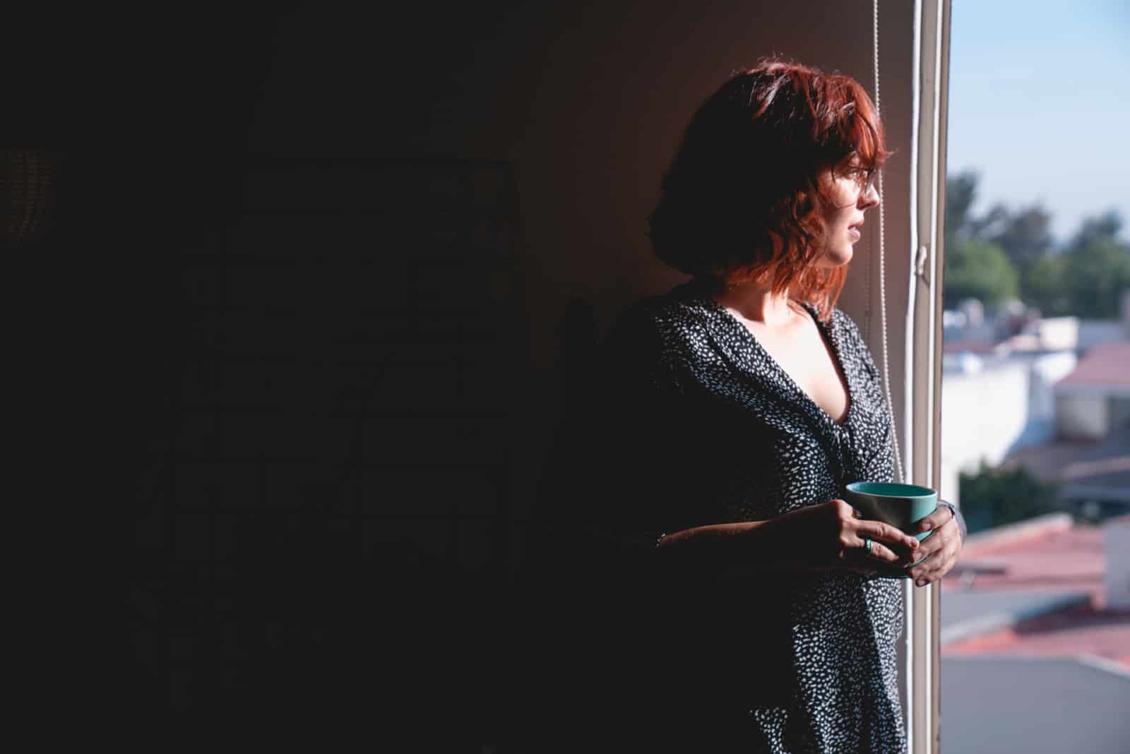 femme tenant un mug en regardant par la fenêtre