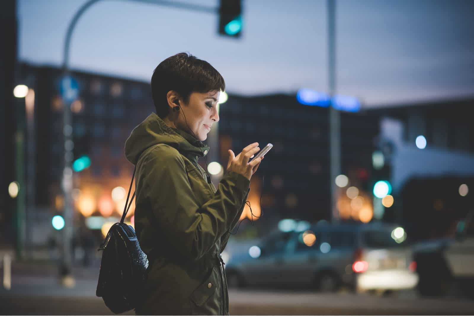 femme tenant un smartphone regardant vers le bas lécran dans la nuit de la ville