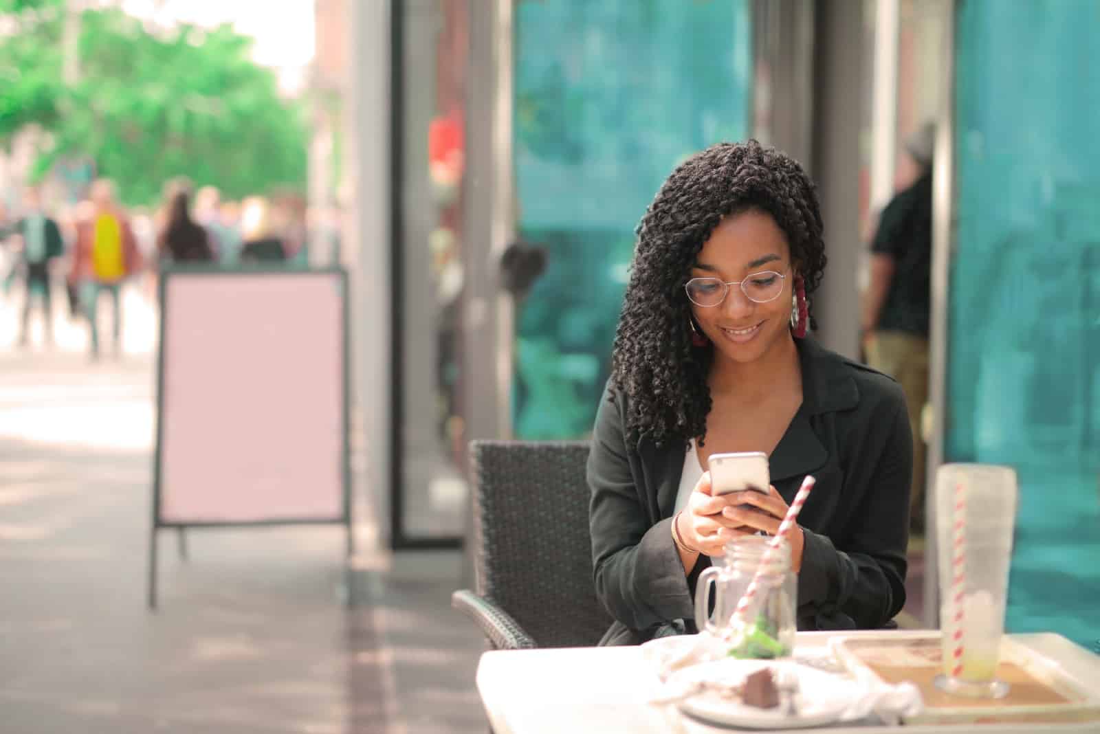 Femme utilisant un smartphone assise dans un café en plein air