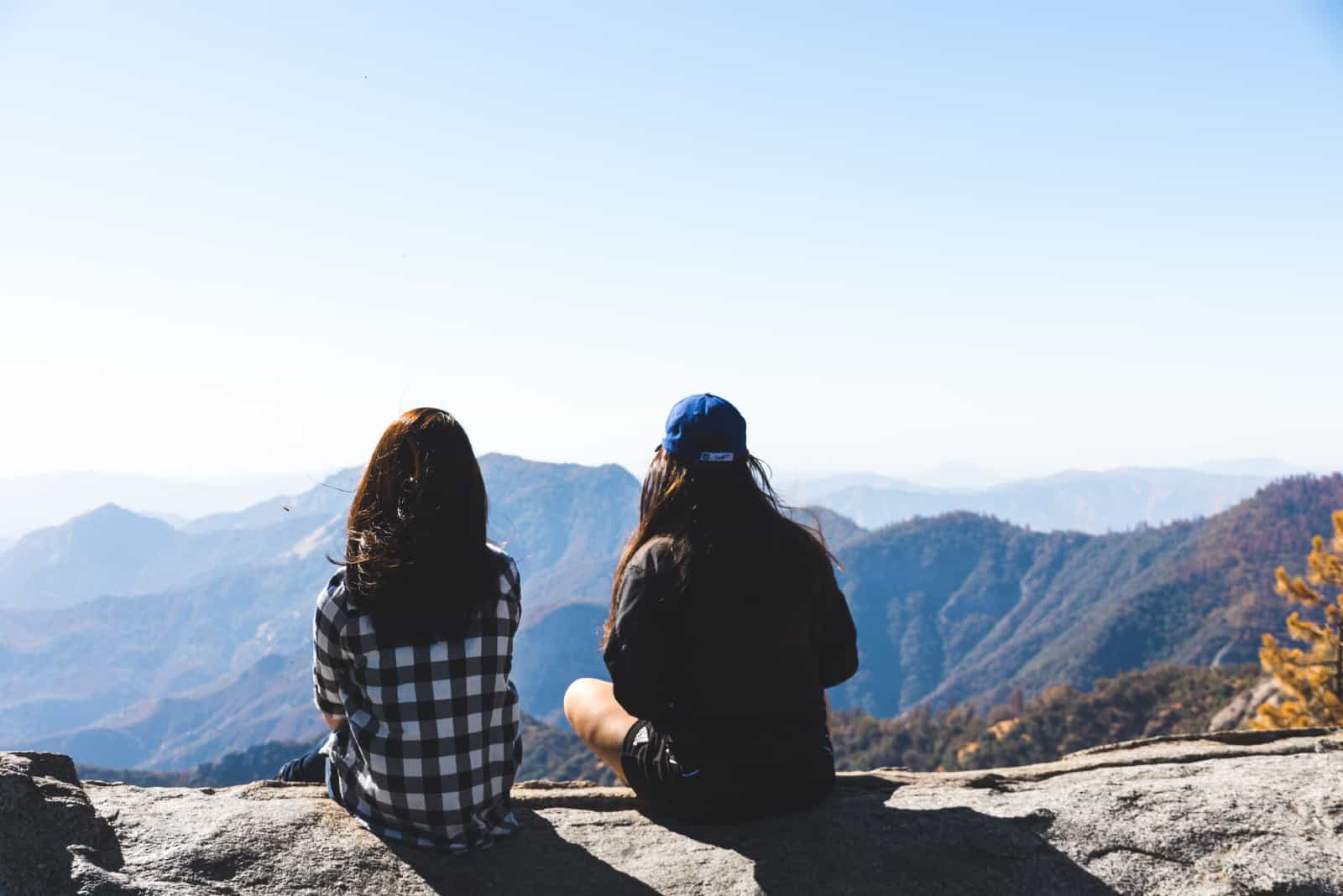 deux femmes assises sur un rocher en regardant la montagne