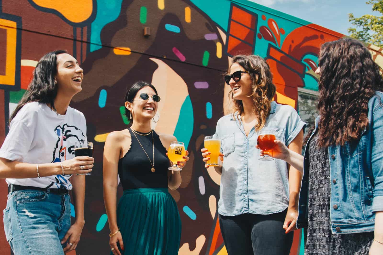 quatre femmes buvant de la bière près d'un mur de graffitis