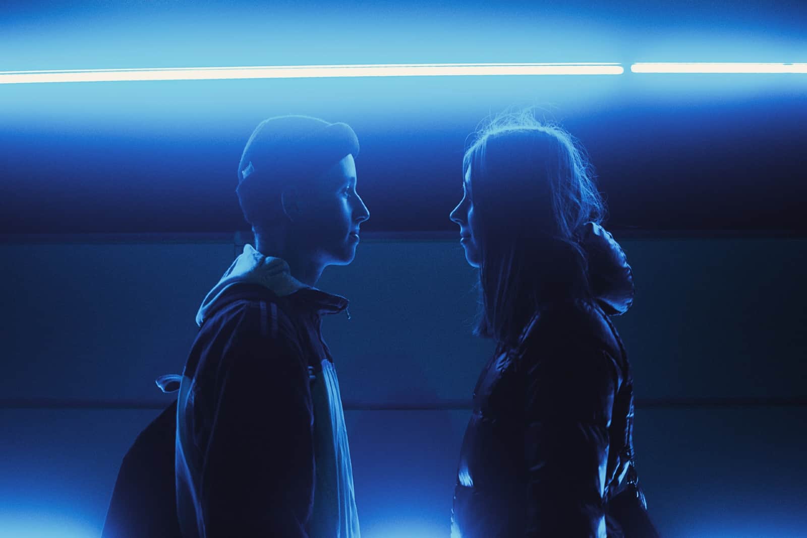 Un homme et une femme se regardent dans les yeux en se tenant près d'un néon
