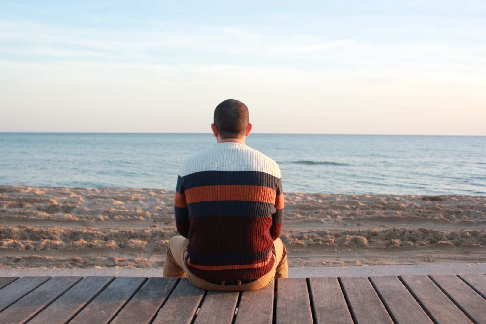 homme regardant la mer assis sur un panneau en bois