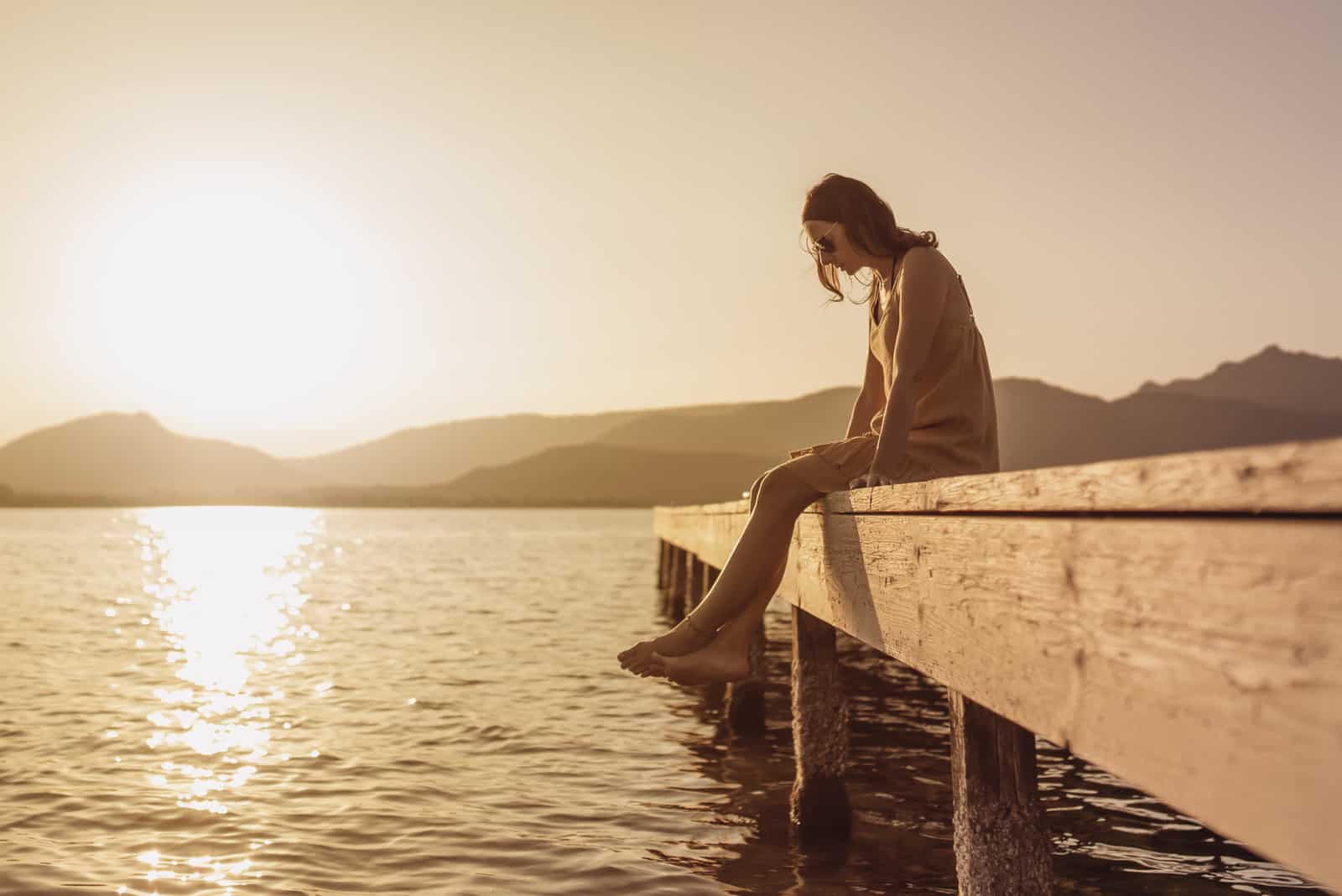 jolie jeune femme assise sur une jetée d'un lac