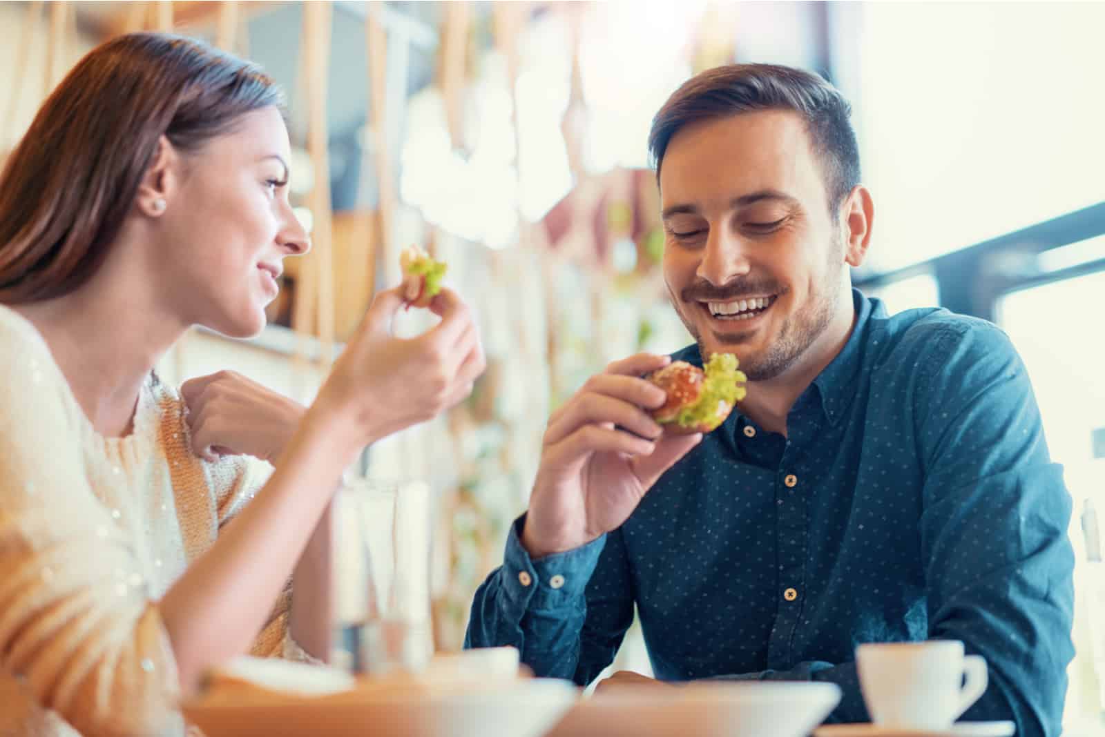 un homme et une femme assis à une table mangeant et riant