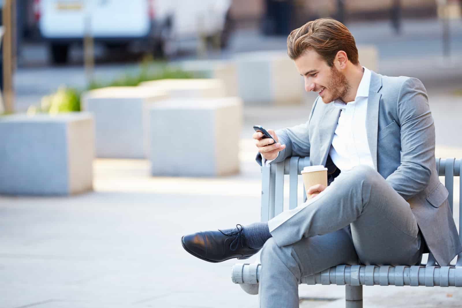 un homme souriant en costume est assis sur un banc et les touches du téléphone