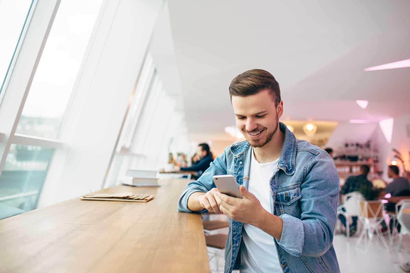 un homme souriant est assis dans un café et tient un téléphone à la main