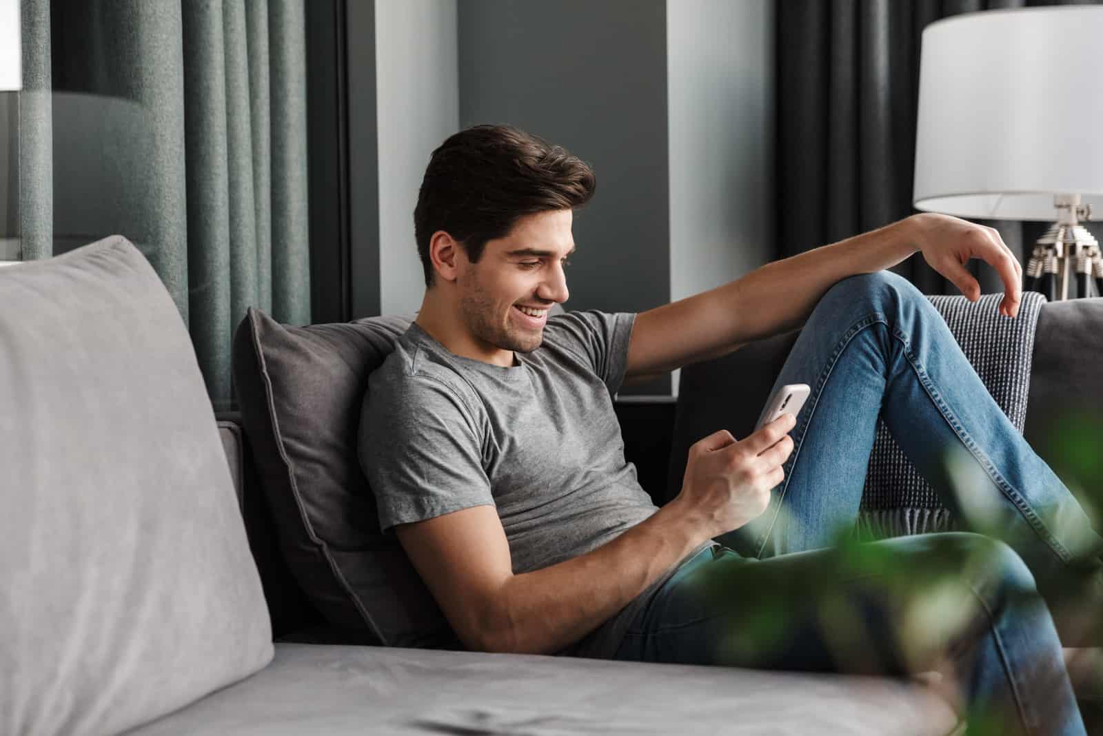un homme souriant est assis sur le canapé et les touches du téléphone
