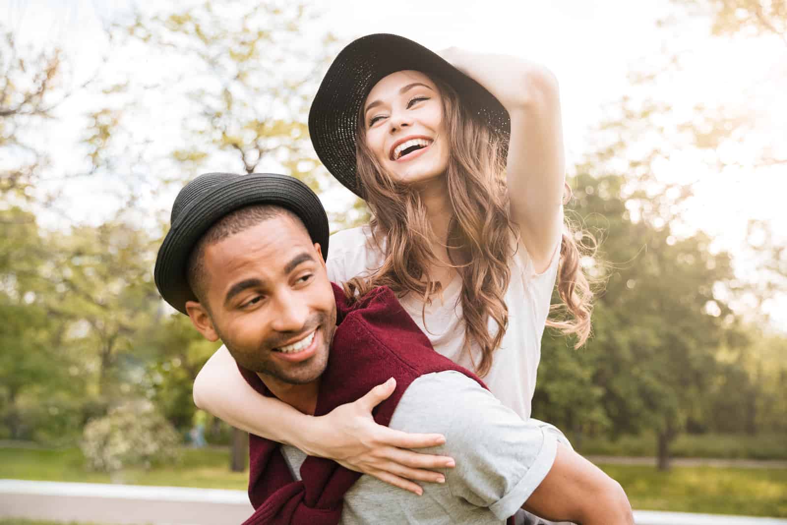 un homme souriant porte une femme avec un chapeau sur la tête