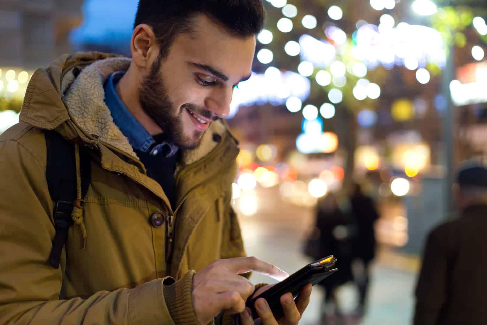 un homme souriant se tient dans la rue tenant un téléphone à la main